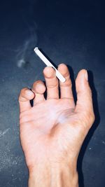 Close-up of hand smoking cigarette against wall