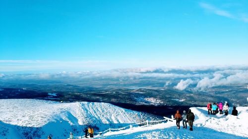 High angle view of people standing on snow covered mountain against blue sky