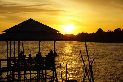 Silhouette built structure by river against sky during sunset