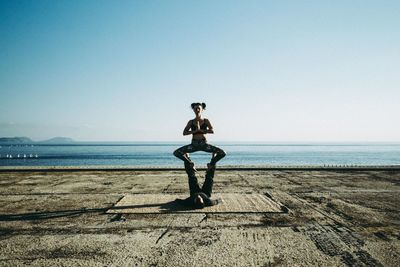 Full length of man balancing woman on feet by sea against clear sky