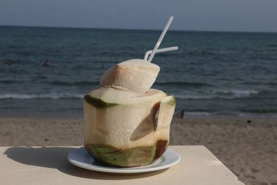 Close-up of coconut water with straw in plate on table at beach