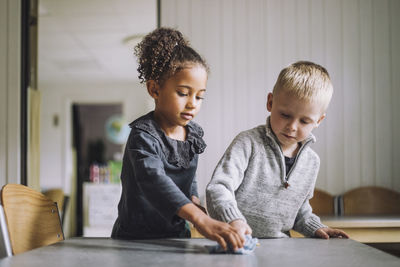 Multiracial male and female students cleaning dining table at kindergarten