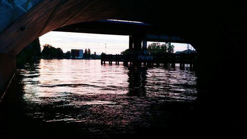 Silhouette bridge over river against sky in city