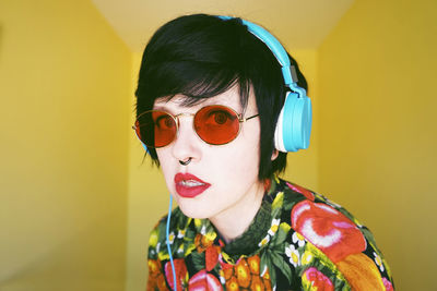 Portrait of hipster woman listening music against yellow wall