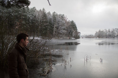 Side view of man standing by lake against sky during winter