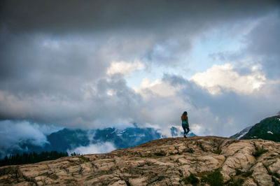 Low angle view of woman walking on rocky hill against cloudy sky