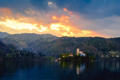 Scenic view of lake by buildings against sky during sunset