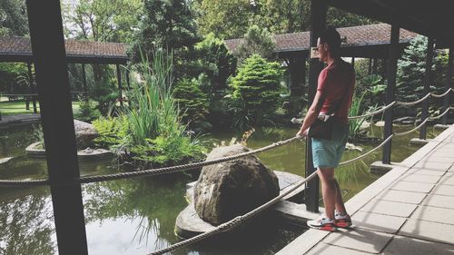 Man standing on footbridge over pond