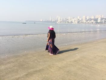 Full length of woman walking on shore at beach in city against sky