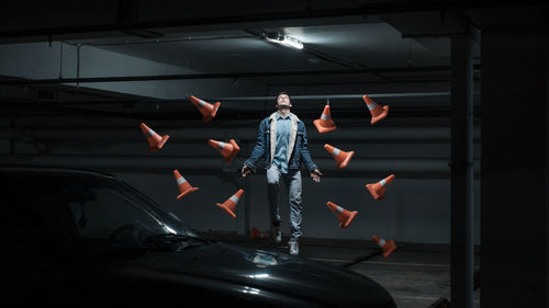 Man levitating by traffic cone s and car in parking lot at night