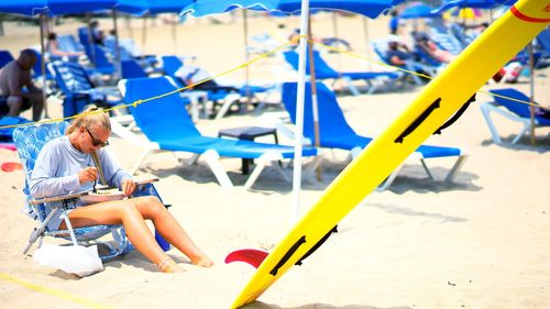 Woman having food while sitting on deck chair at beach