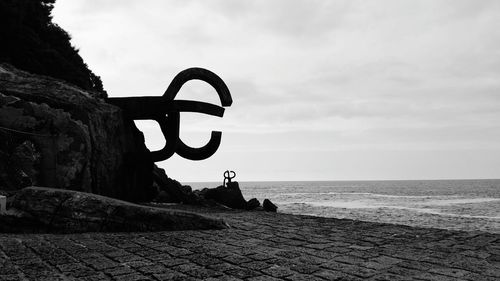 Silhouette sculpture by sea against sky