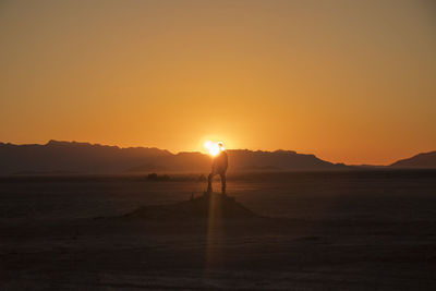 Silhouette person standing on land against sky during sunset