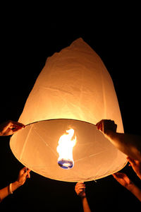 Close-up of hand holding illuminated lantern against black background