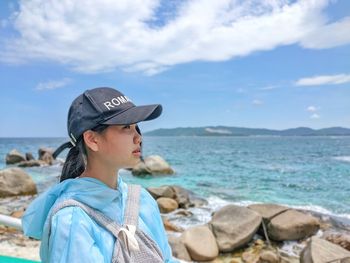 Man wearing hat on rock at beach against sky