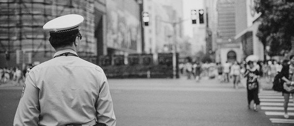 Rear view policeman looking at people walking on street in city