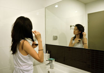 Woman making hairstyle while reflecting of mirror in bathroom