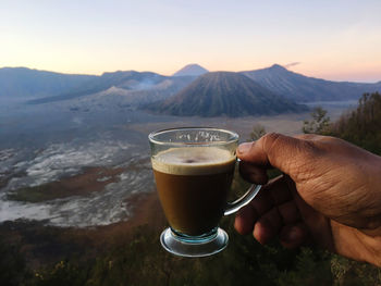 Cropped hand holding coffee cup against mountains