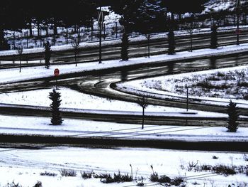 Snow covered road by trees on field during winter