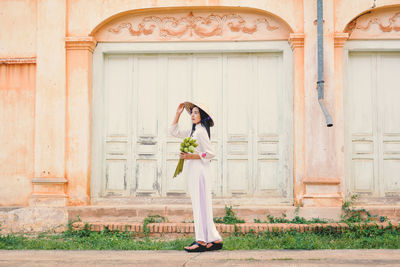 Side view of vietnamese woman standing against built structure