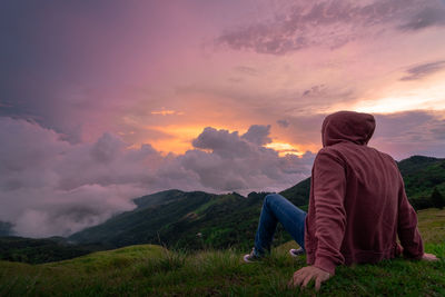 Rear view of man sitting on land against sky during sunset