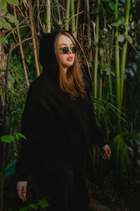 Portrait of young woman standing against plants