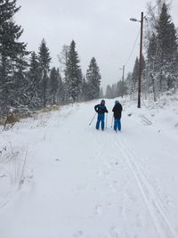 Rear view of friends skiing on snow covered field against sky