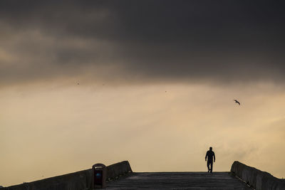 Silhouette people standing on bridge against sky during sunset