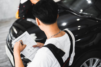 High angle view of mechanic with document analyzing car at auto repair shop