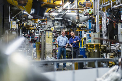 Mature male professionals examining machines while standing in industry