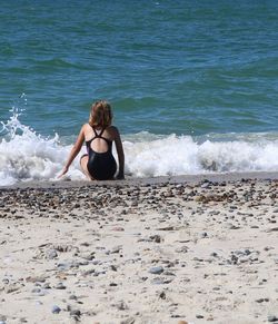 Rear view of woman crouching at beach during sunny day
