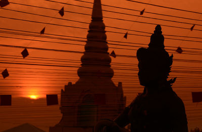 Silhouette statue with religious structure against sunset