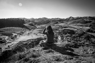 Rear view of woman sitting on mountain against clear sky