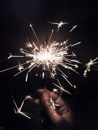 Cropped hand holding lit sparkler at night