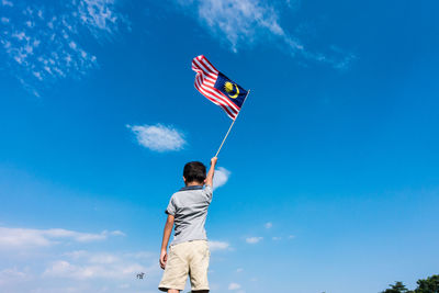 Low angle view of boy holding flag while standing against blue sky