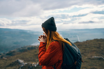 Person wearing hat standing on mountain against sky