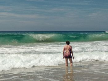 Rear view of man standing at beach against sky