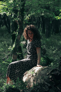 Full length of woman sitting on tree in forest