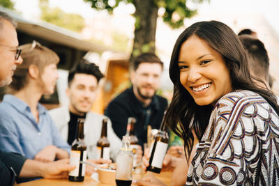 Portrait of smiling young woman sitting with friends and enjoying at social gathering
