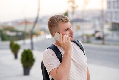 Handsome blond bearded serious man wearing backpack,casual clothes,having call using smartphone 