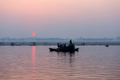 People in boat on river against sky during sunset