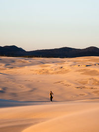 Woman walking on sand against sky during sunset