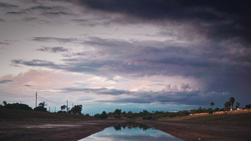 Road by river against sky at sunset