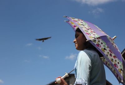 Low angle view of girl holding umbrella against blue sky