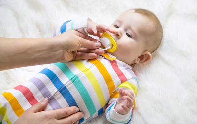 Mother holding pacifier while baby lying on bed