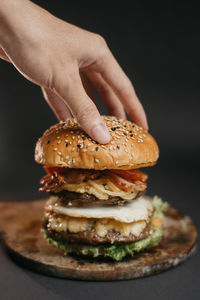 Close-up of hand holding burger against black background