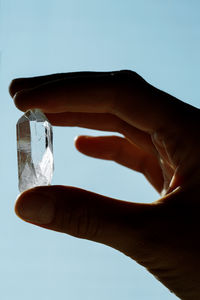 Hand holding crystal against blue sky