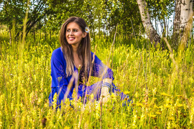 Smiling young woman looking away while sitting by flowering plants