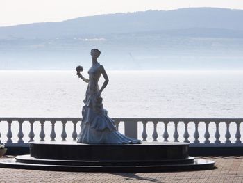 Man standing on railing by sea against sky