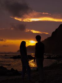 Silhouette friends on beach against sky during sunset